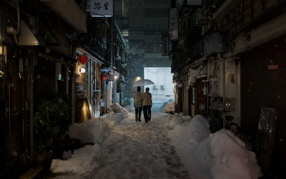 A couple under an umbrella in a snowy lantern-lit alley in Kanazawa