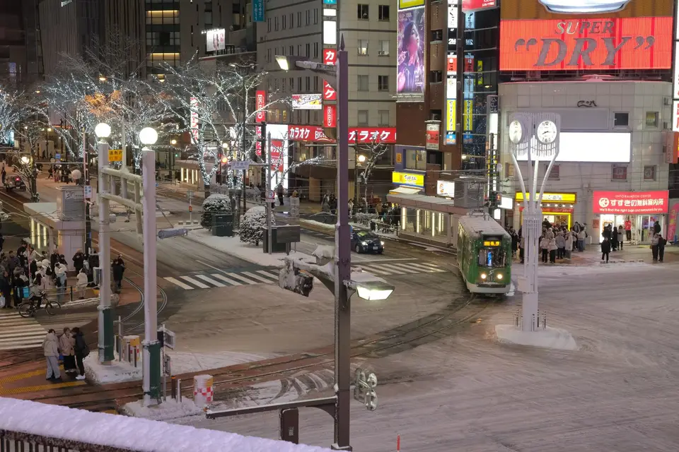 A tram passing lit-up trees on a snowy Sapporo street at night
