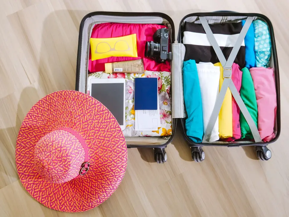 An open suitcase packed with clothes, a camera and a sun hat
