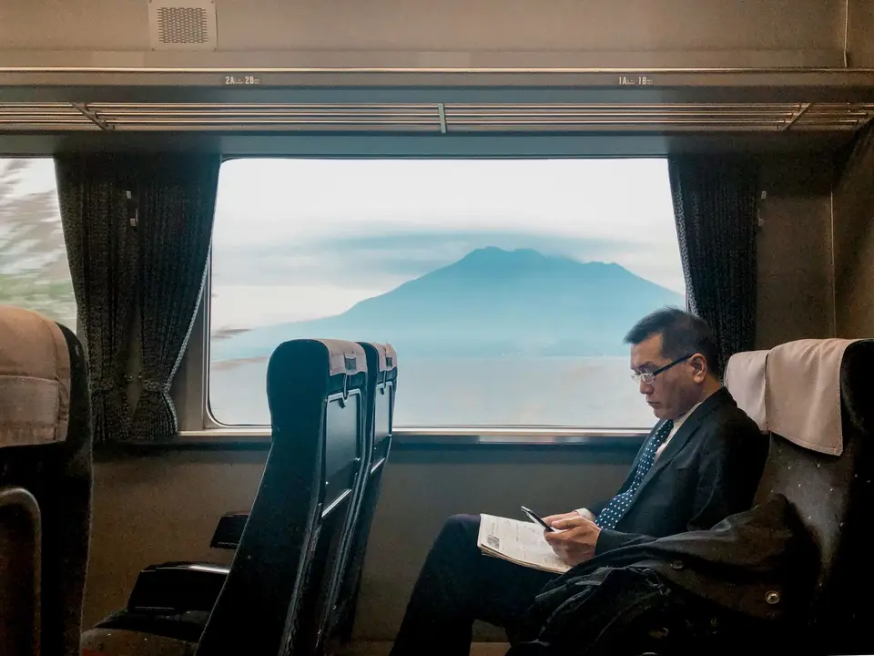 A passenger reading on a train with Mount Fuji visible through the window